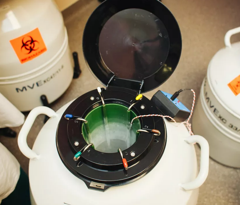 An open MVE XC 34/18 Storage Tank by Chart/MVE reveals metal canisters inside, used for holding up to 2100 straws for 18 weeks. A biohazard label is visible on a nearby container. The tank features a five-year vacuum warranty.