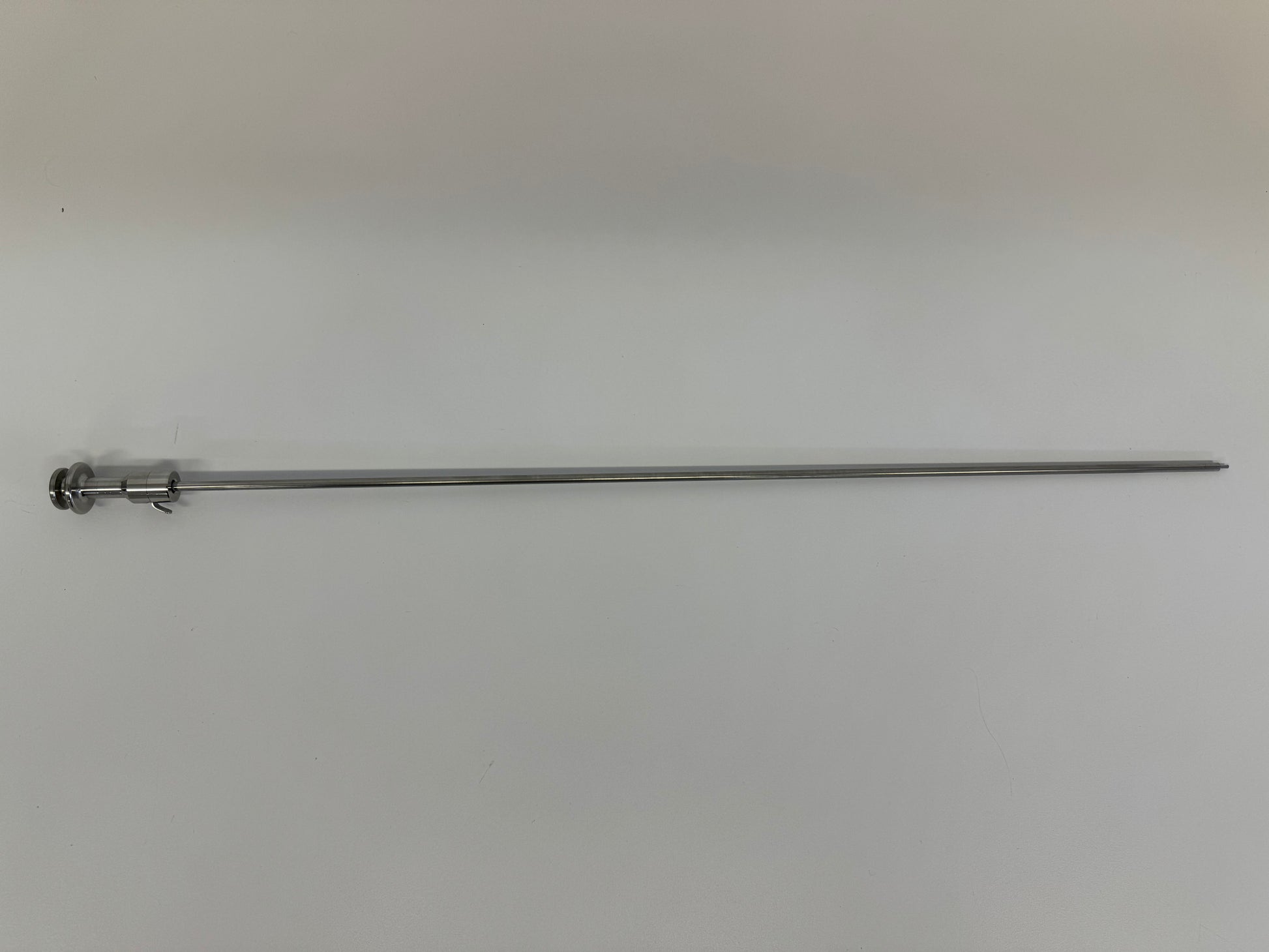 A slender metal rod from the RR AI Kit—With Electric Thaw Unit, featuring a small circular handle and end clip, lies horizontally on a plain, light surface.
