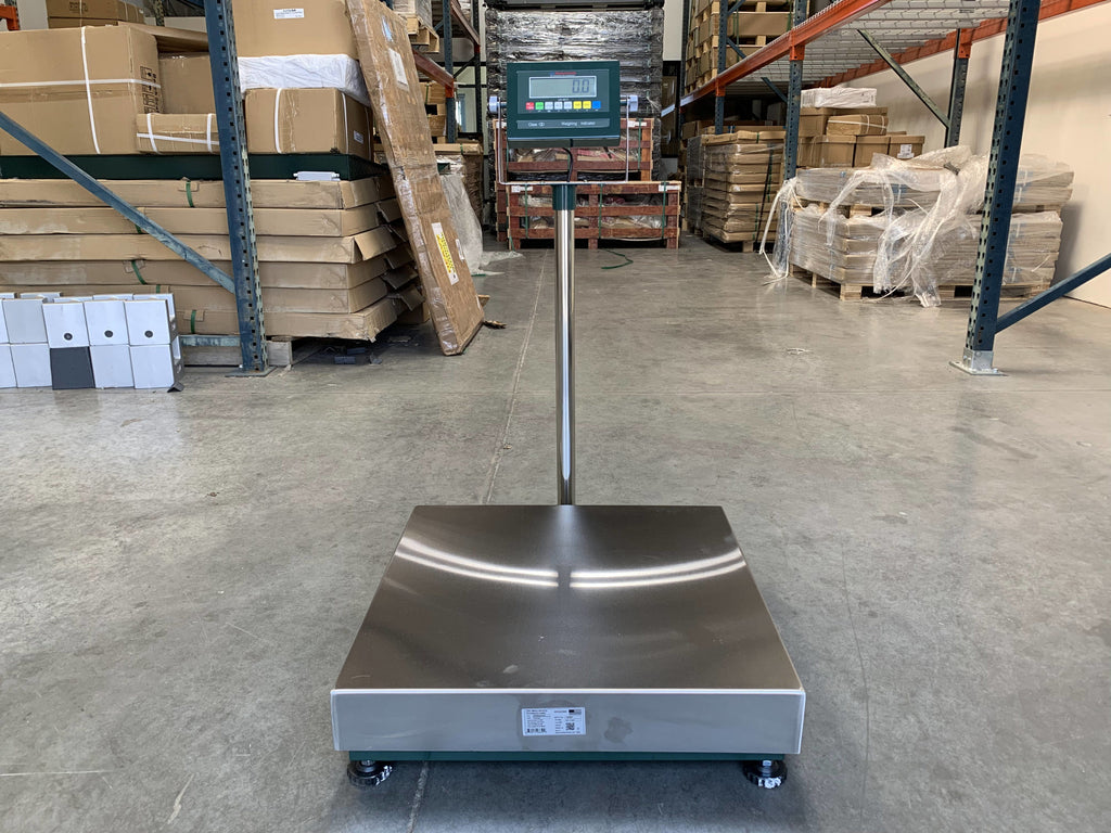 A Semen Tanks - Select Genetics Bench Cryo-Alert Scale 24"x24" with US-6011 Indicator and Stacklight (90 lbs) is on wheels in a warehouse, surrounded by shelves with boxes and pallets.
