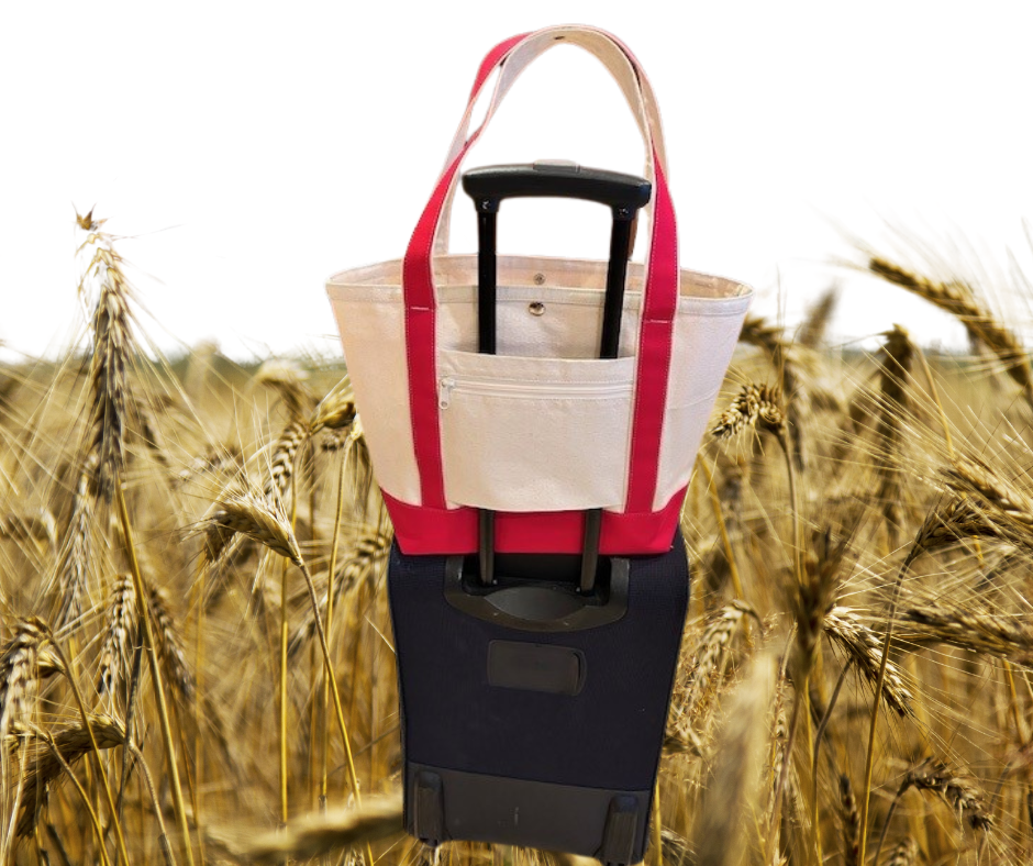 The Semen Tanks - Select Genetics Totes for Everyday Use, featuring 18 or 24 inch straps, sits on a navy rolling suitcase in a wheat field. Its extra roomy interior holds all your essentials—perfect for daily use.