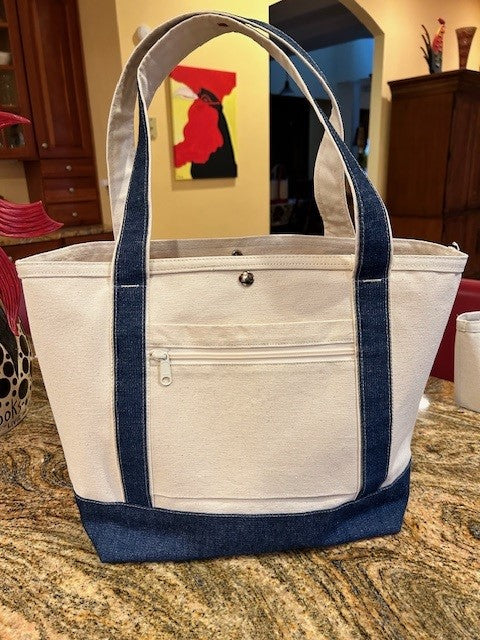 A beige Semen Tanks - Select Genetics Totes for Everyday Use with blue denim accents and 18 or 24 inch straps sits on a kitchen counter. It features a front zipper pocket, button closure, and a bright painting in the background.
