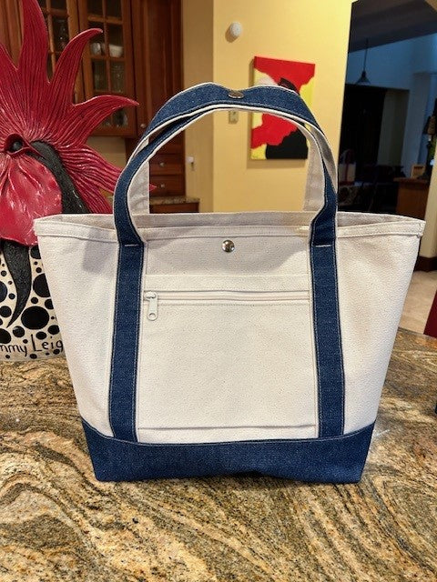 A Semen Tanks - Select Genetics Totes for Everyday Use with denim accents and 18 or 24 inch straps rests on a kitchen counter, featuring a front zipper pocket, snap closure, and can slide over rolling luggage handles.
