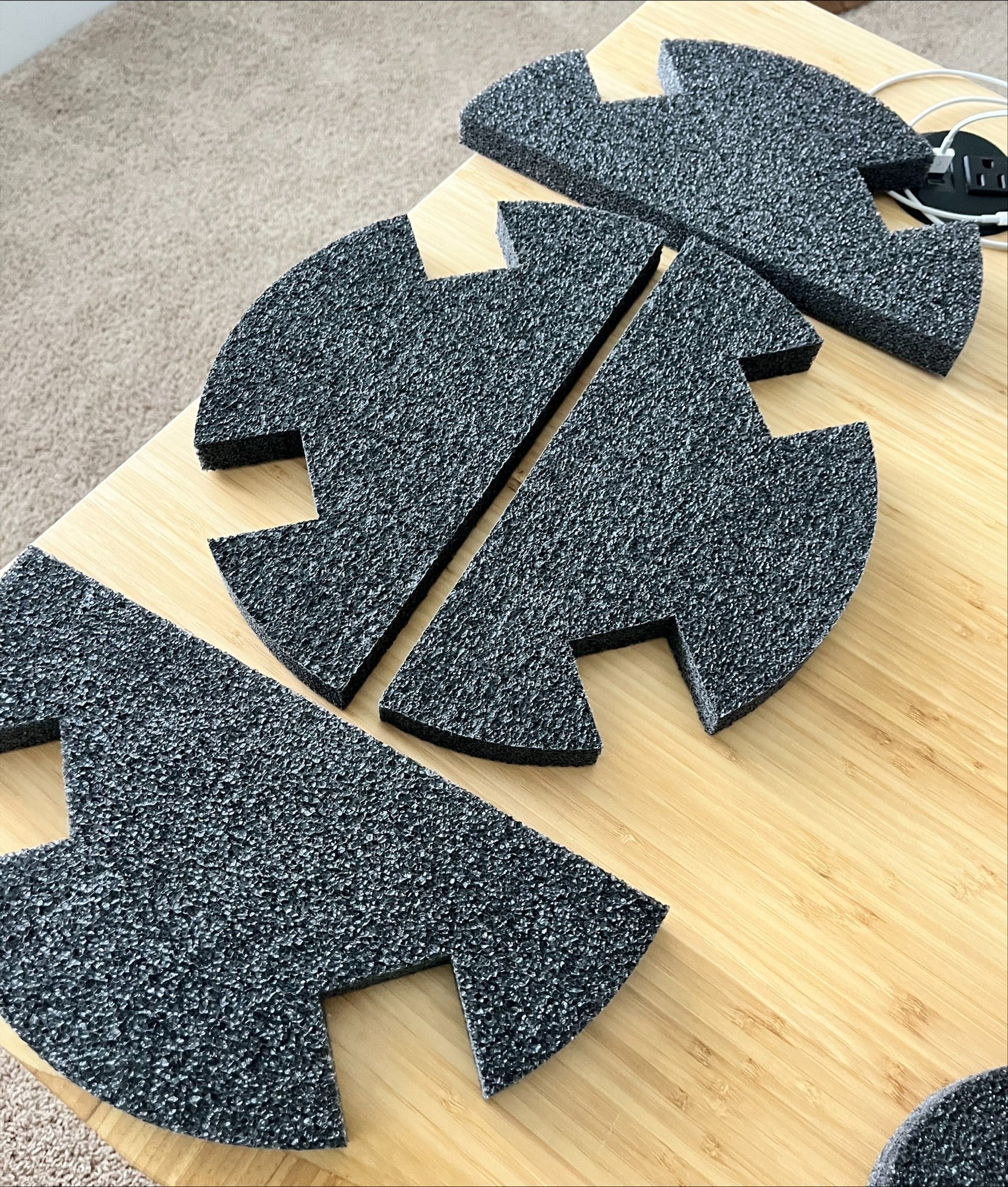 Four black foam replacement pieces from the Chart/MVE TOTAL KIT (SIDES, TOP, and BOTTOM) for 4/2 & 4/3 V mushroom MVE Protective Shipping Containers are arranged on a light wooden surface, with part of a carpet visible in the background.