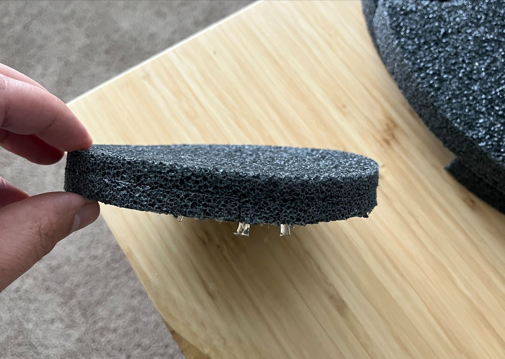 A hand holds a Chart/MVE Foam Replacement Piece for MVE Protective Shipping Container (Top Piece) with small metal pins, resting on a light wooden surface. Another similar top piece is partially visible in the background.