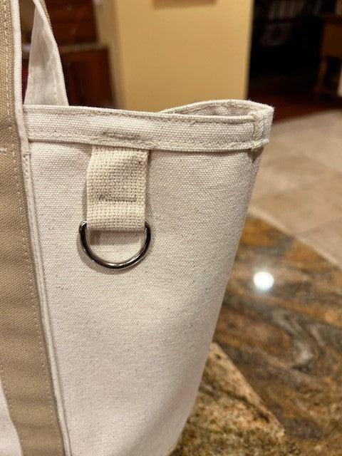 Close-up of a Semen Tanks - Select Genetics beige-accented duck canvas tote for everyday use, with a fabric loop and silver D-ring, shown on a stone-patterned countertop. Available with 18 or 24 straps.
