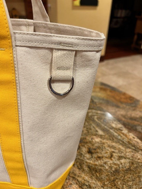 A close-up of the Semen Tanks - Select Genetics Totes for Everyday Use with yellow accents and 24 inch straps, featuring a metal D-ring near the top, resting on a brown and tan granite countertop.