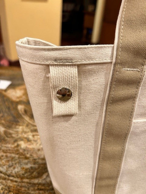 Close-up of the Semen Tanks - Select Genetics Totes for Everyday Use, Beige Accent, with 18 or 24 inch straps, made from high quality duck canvas and featuring a fabric loop and metal snap button. Background is slightly blurred.