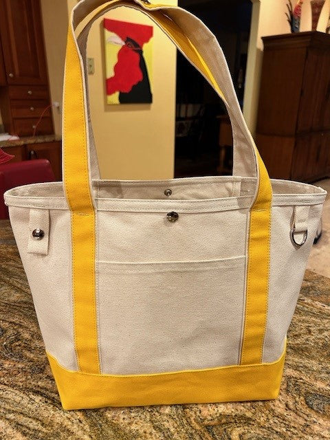 A Semen Tanks - Select Genetics Totes for Everyday Use bag with yellow accents and 24-inch straps stands upright on a kitchen counter. Made in the USA, it features a front pocket with snap button.