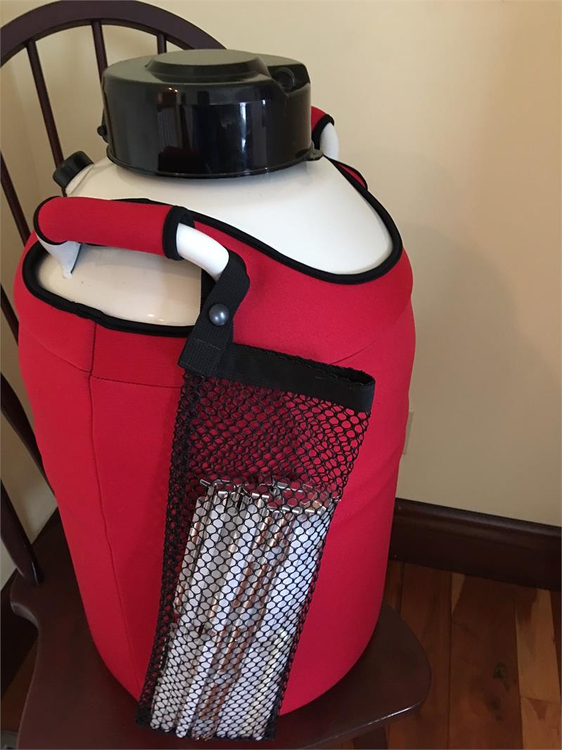 The Chart/MVE MVE XC 20 Signature Tank PLUS Canekeeper sits on a wooden chair by a cream wall. The large white tank with black lid fits inside the bright red insulated Cane Keeper cover, which features a black mesh pocket for storage. Ships free.